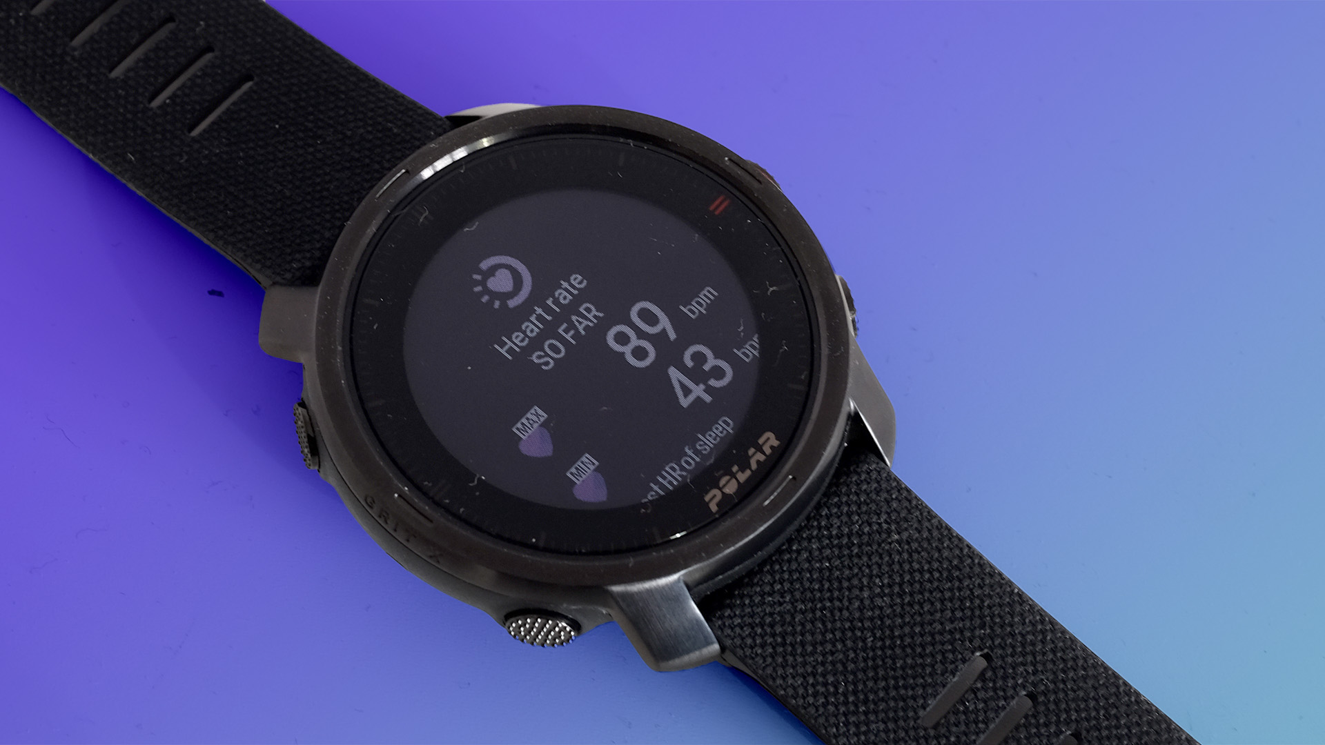 The Polar Grit X on a purple background with the screen displaying the heart rate.
